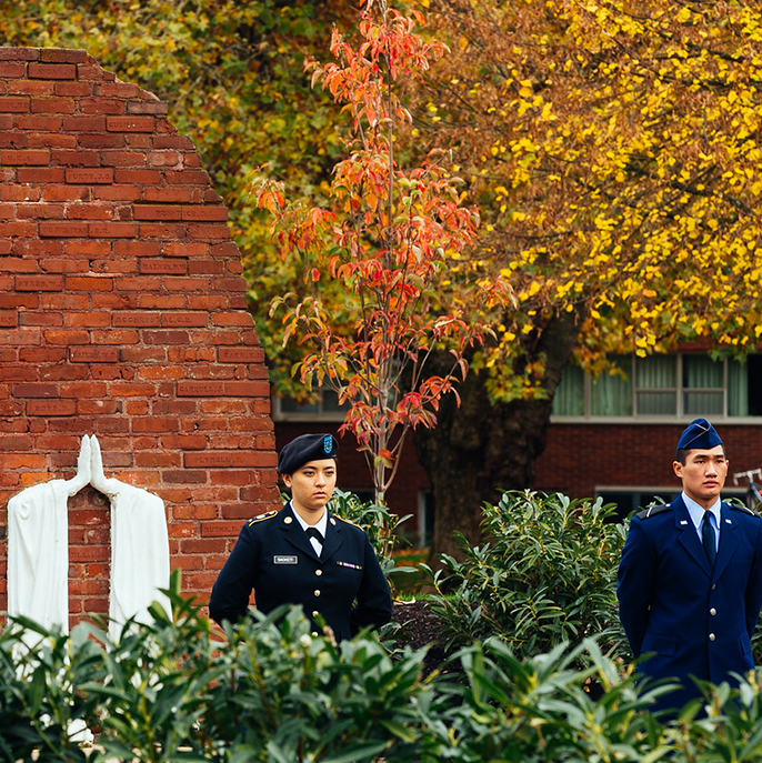 two students in uniform stand guard in front of memorial