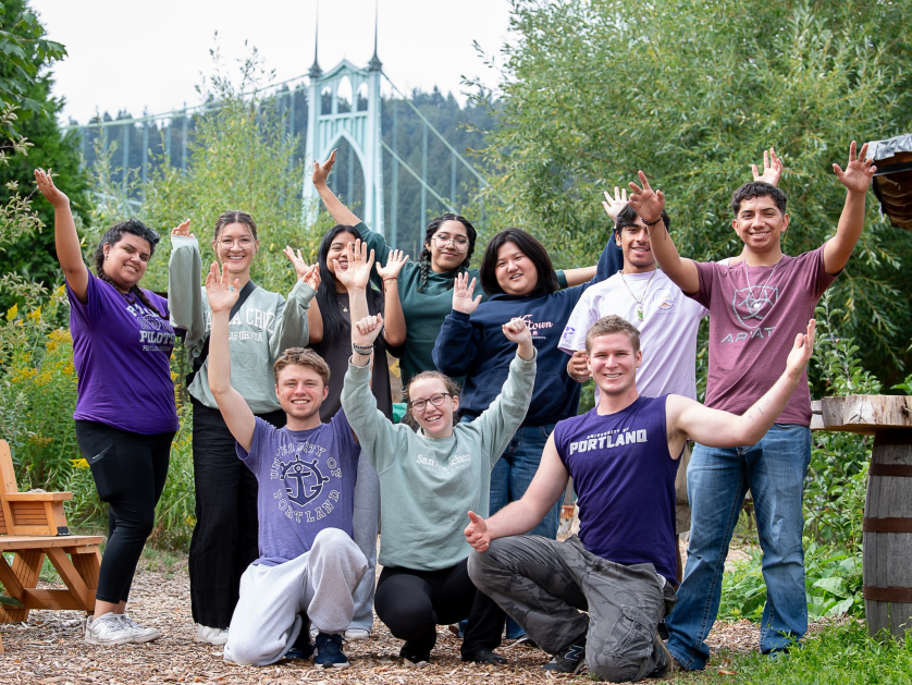 A gathering of students standing closely together, all smiling as they pose for a group photo with the St Johns bridge in the background.