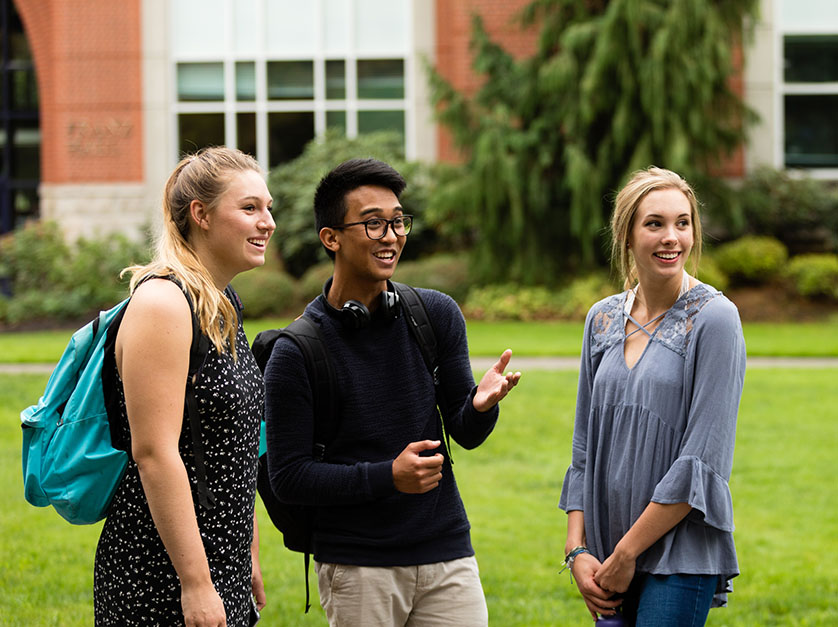 Three students smile and talk on University of Portland's campus