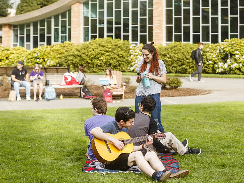 A group of students playing guitar, talking and doing various activities in the quad of University of Portland