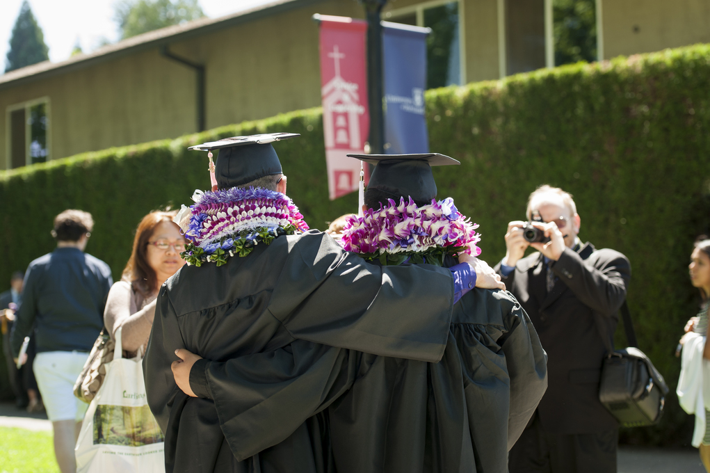 Two students in commencement cap and gown, facing away from the camera