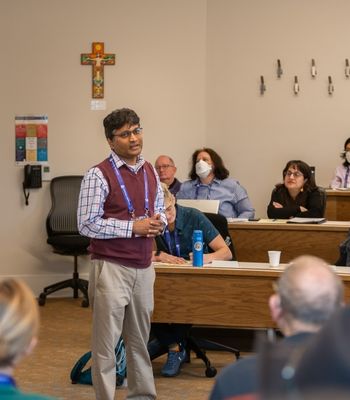 A lecturer in a classroom speaks in front of a group of people listening intently