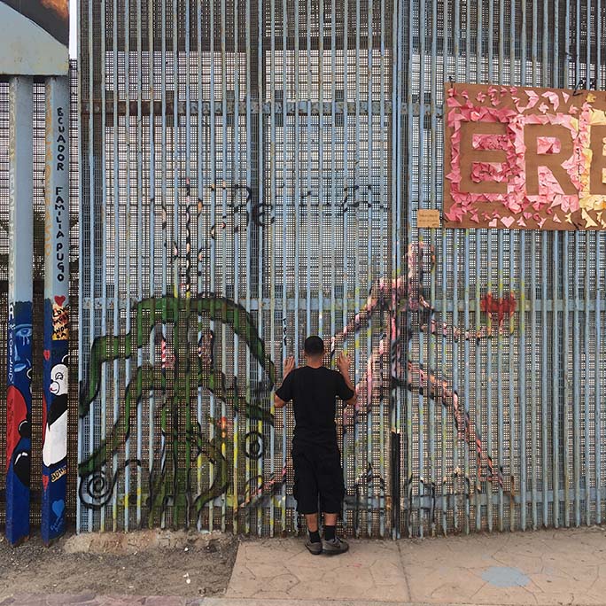 Person looking through a section of the border wall that has artwork of a person running on it.