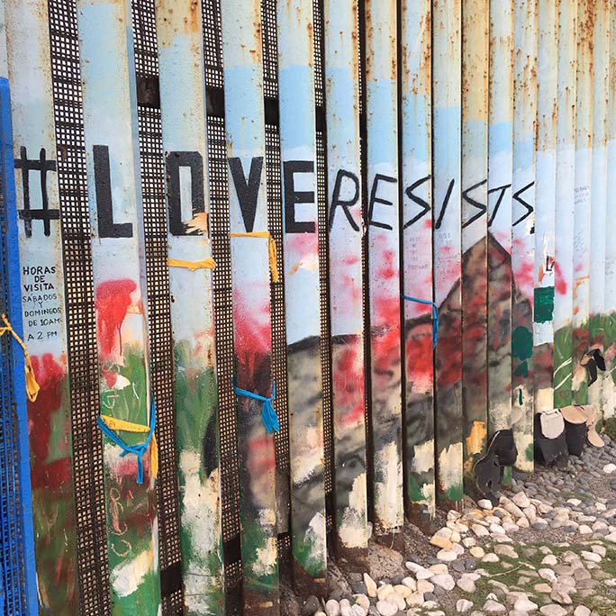 Border wall with the words love resists written upon it.