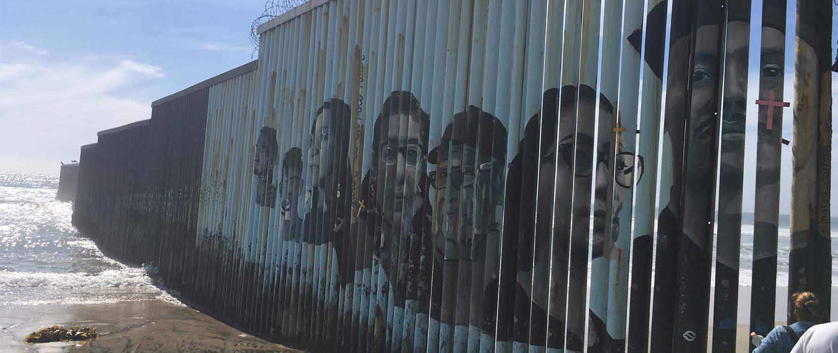 Portraits along the border wall as it leads into the ocean.