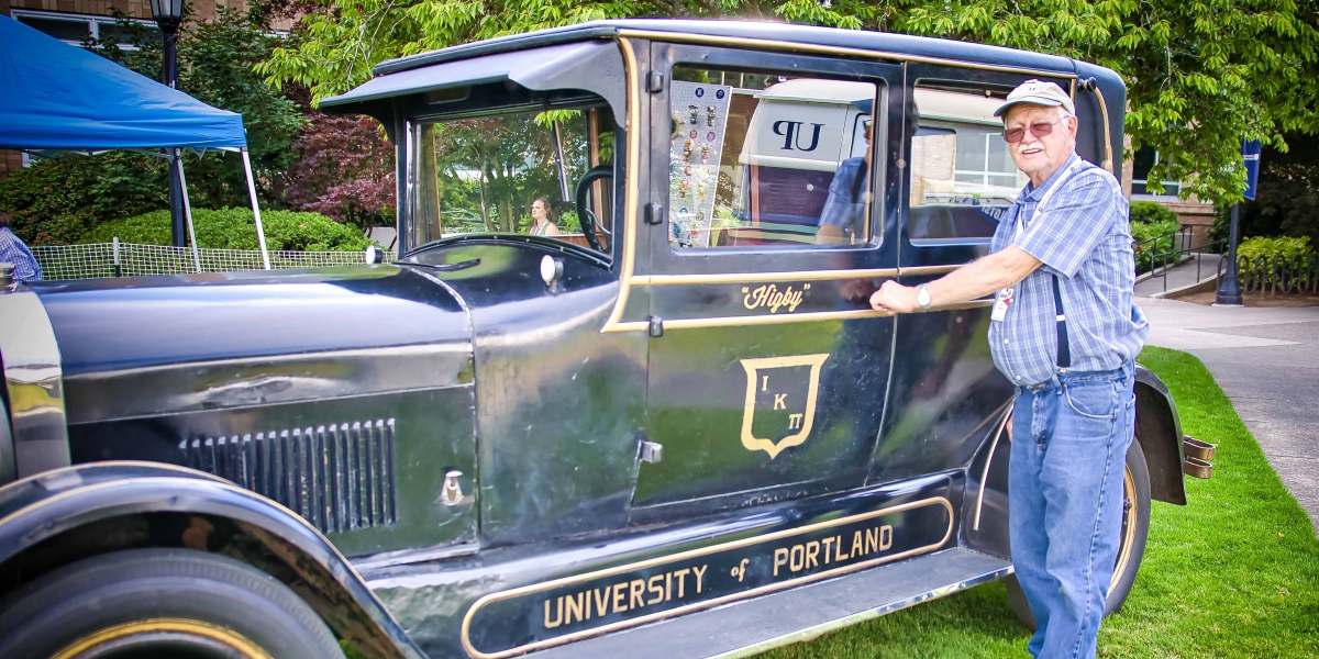 A nice man stands in front of an antique car called Higby.