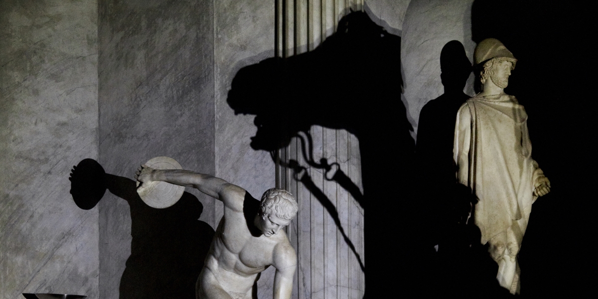 The shadow of a stallion comes between a discus thrower and the god Hermes in the Hall of the Chariot.