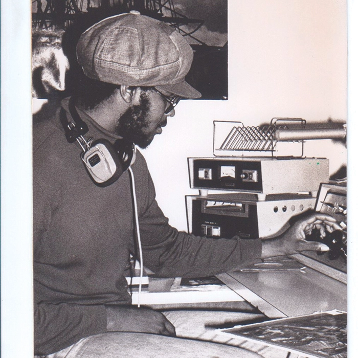 A vintage black and white photograph from 1977  man sits at the soundboard of a college radio station.