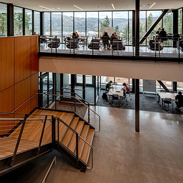 The interior of the Shiley-Marcos center, showing the open floor plan with two levels over looking the Willamette River with a wall of windows 