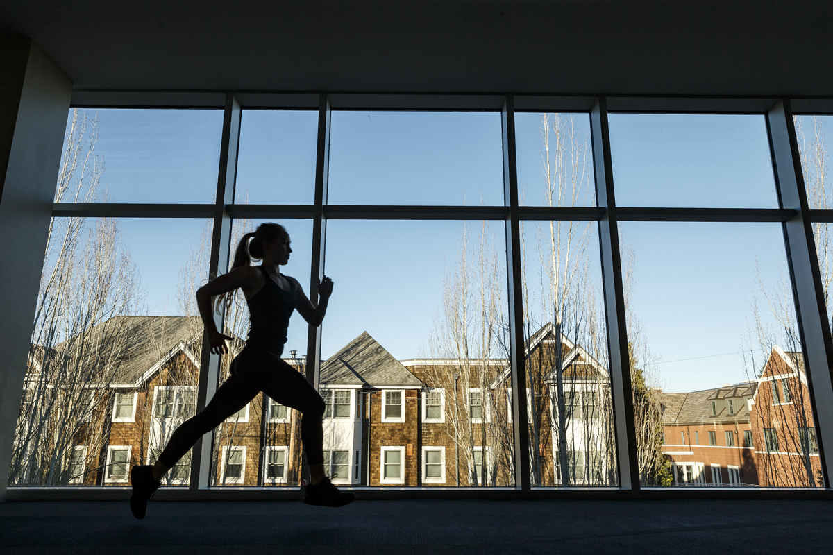 Student running on indoor track with glass showing outdoors