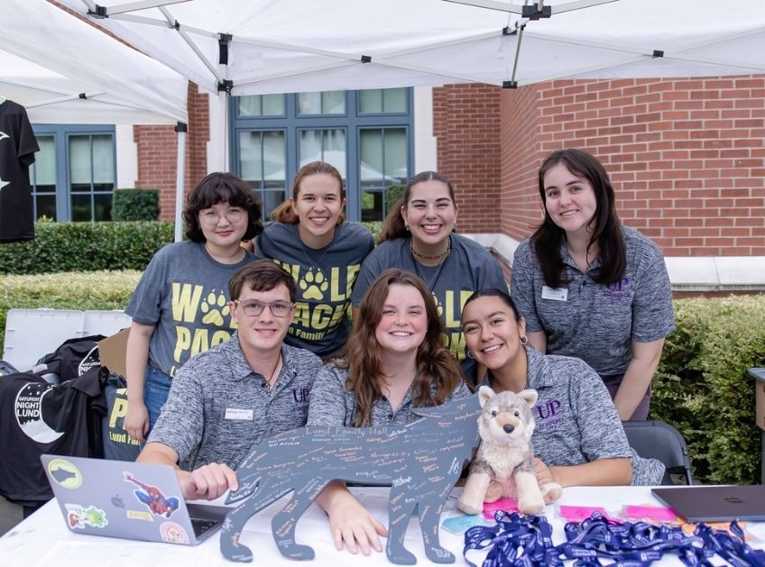 Smiling students at a table welcoming new students to a residence hall