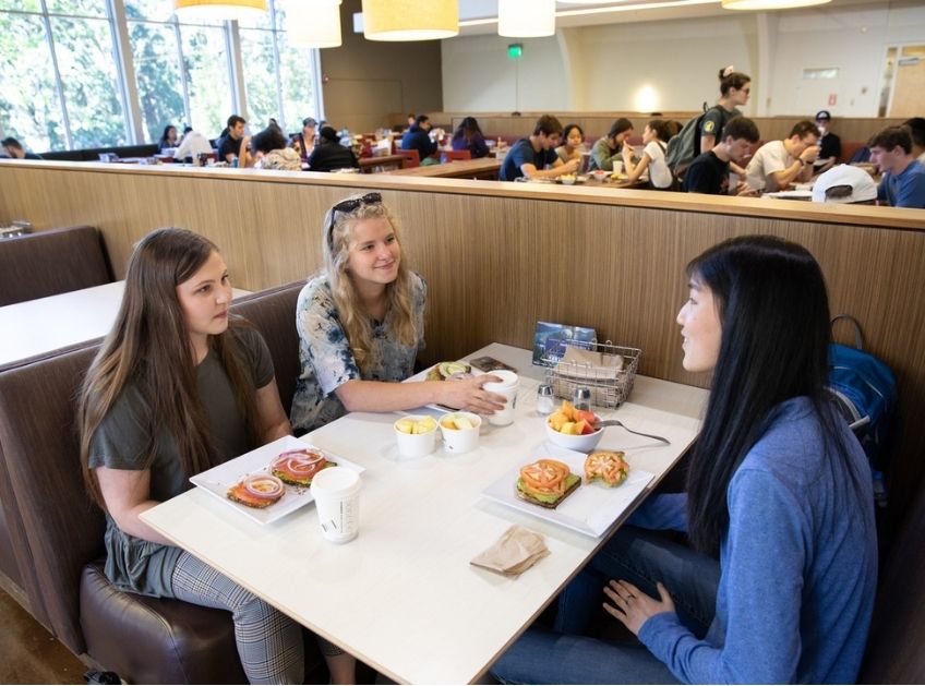 Students eat and converse at a table in the dining hall